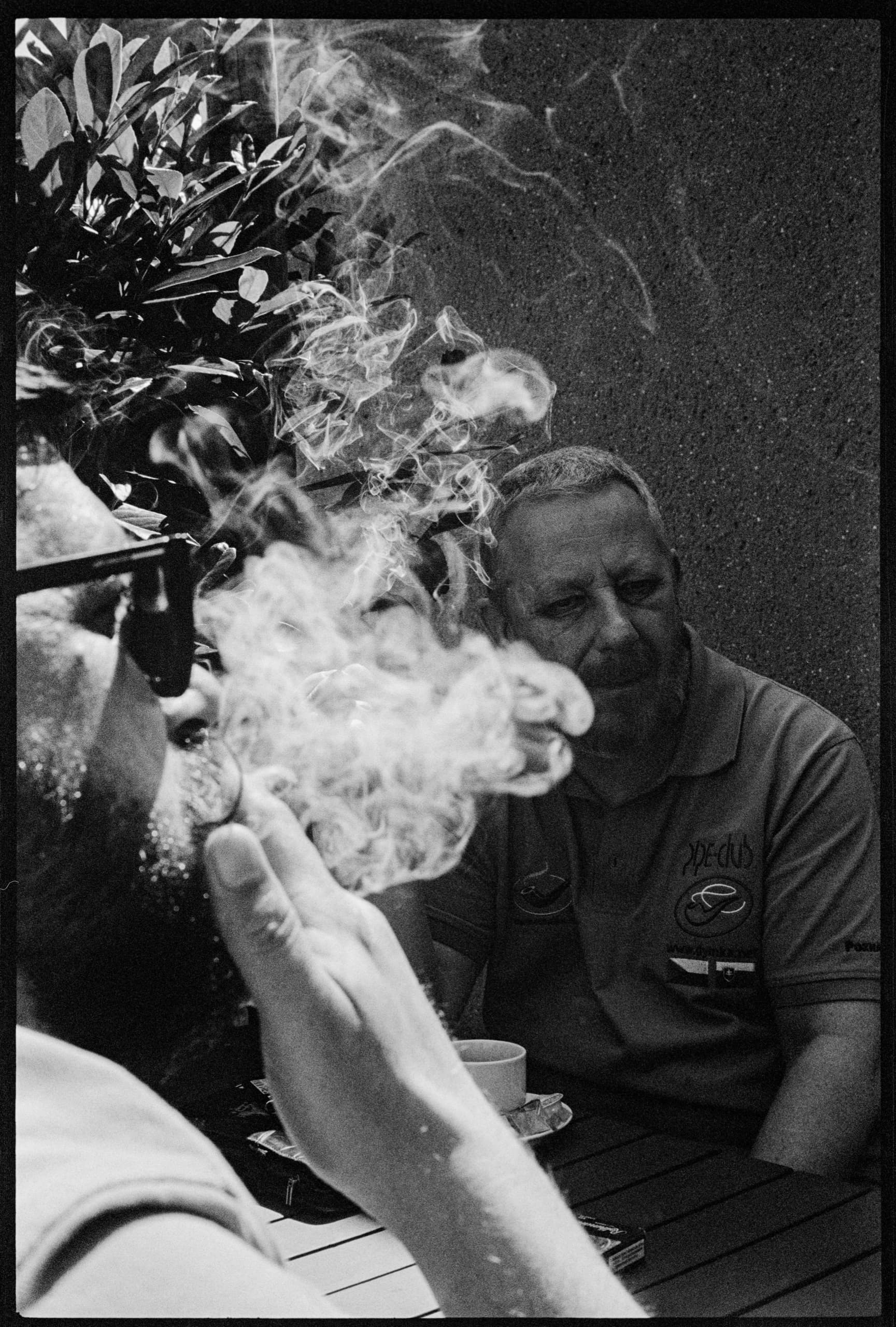 Dva muži u stolu, mezi nimi kouř z cigarety