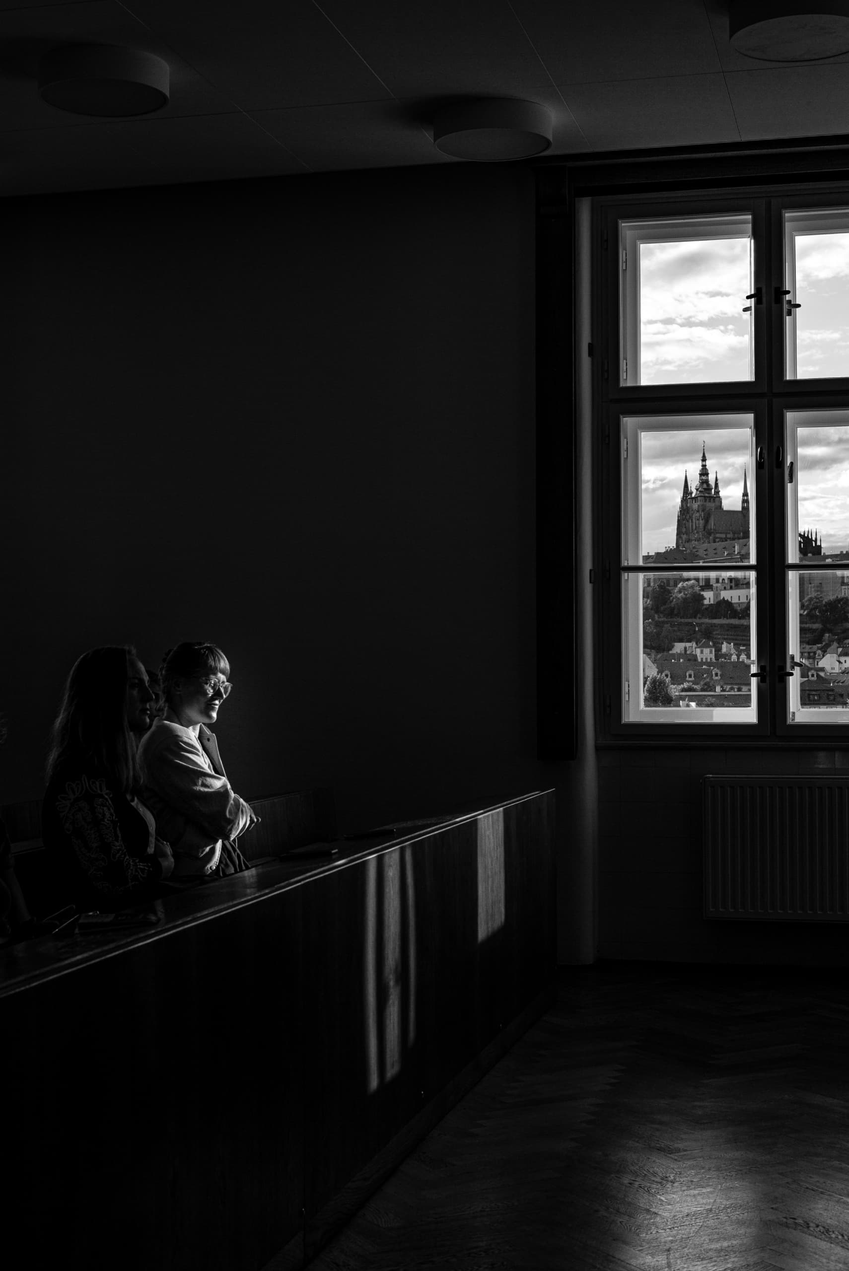 Dva lidé u okna s výhledem na Pražský hrad