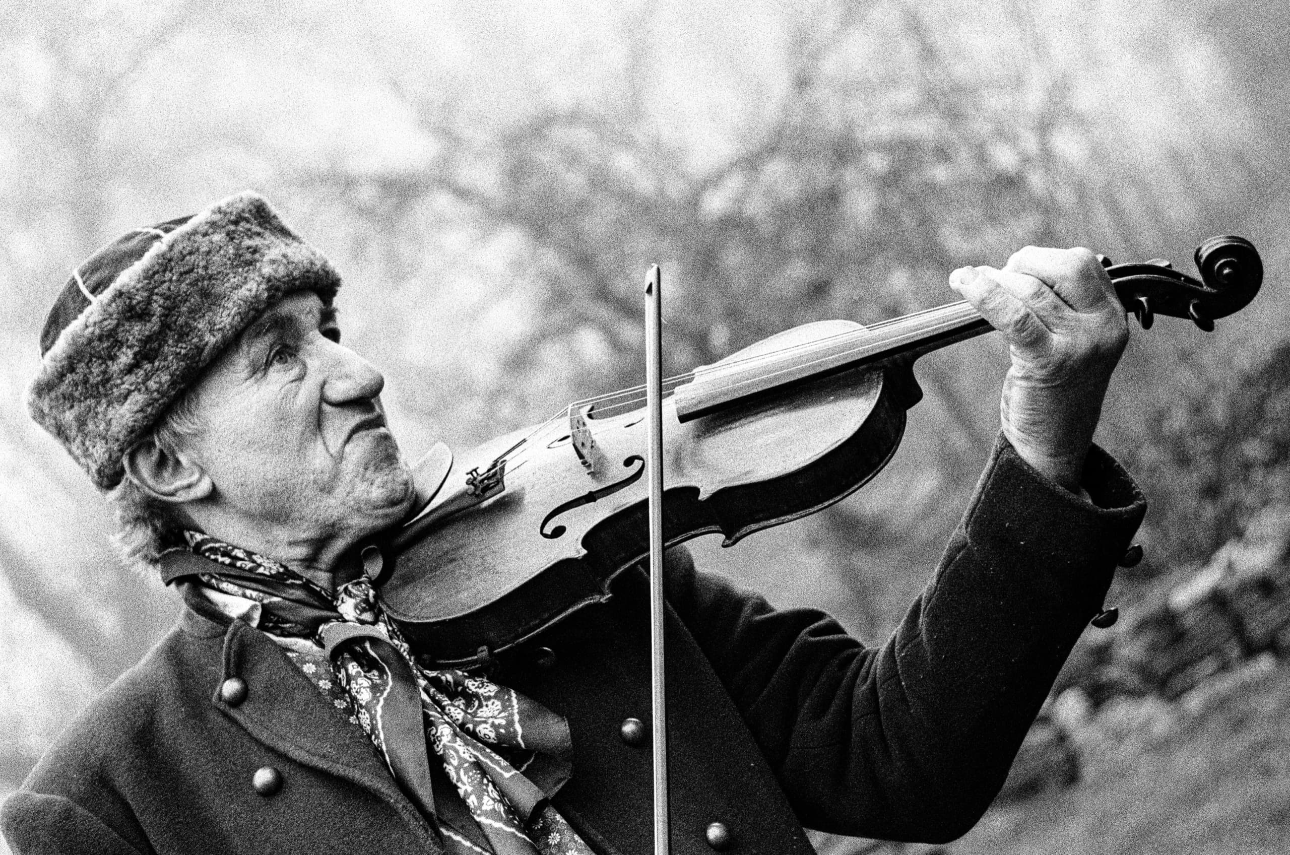 Starší muzikant v beranici hraje na housle